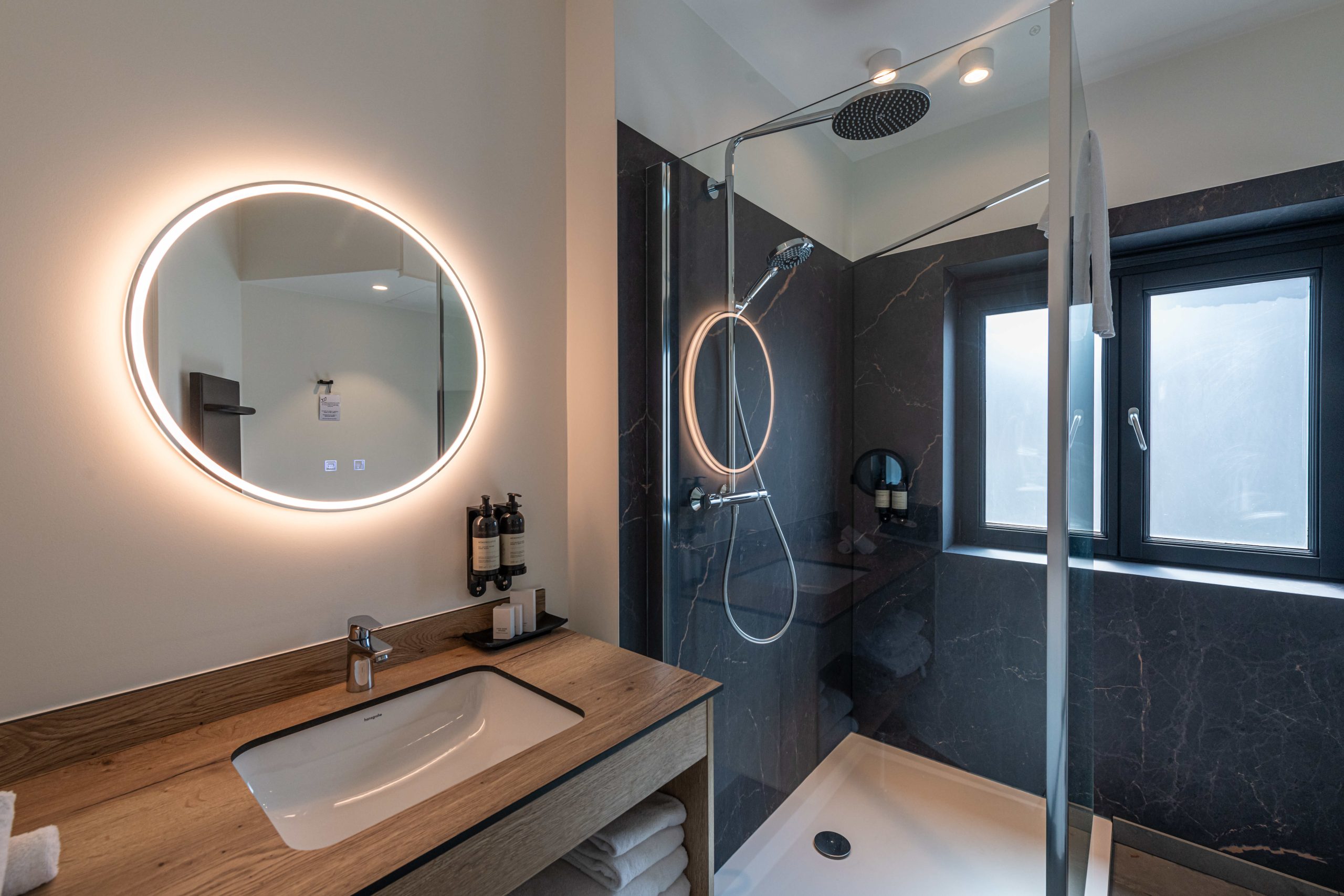Badkamer met regendouche, ronde spiegel en donker marmer